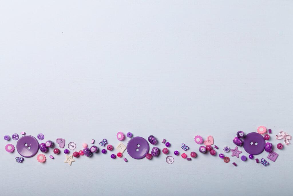 Beads and buttons for sewing and embroidery. Purple set of materials for handcraft, making of bijouterie and accessories. White background, copy space.