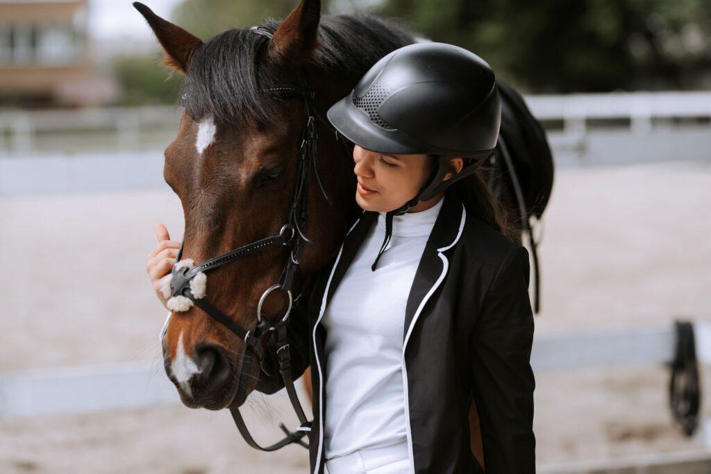Young female rider in formal riding attire gently holding her equitation horse at a training arena
