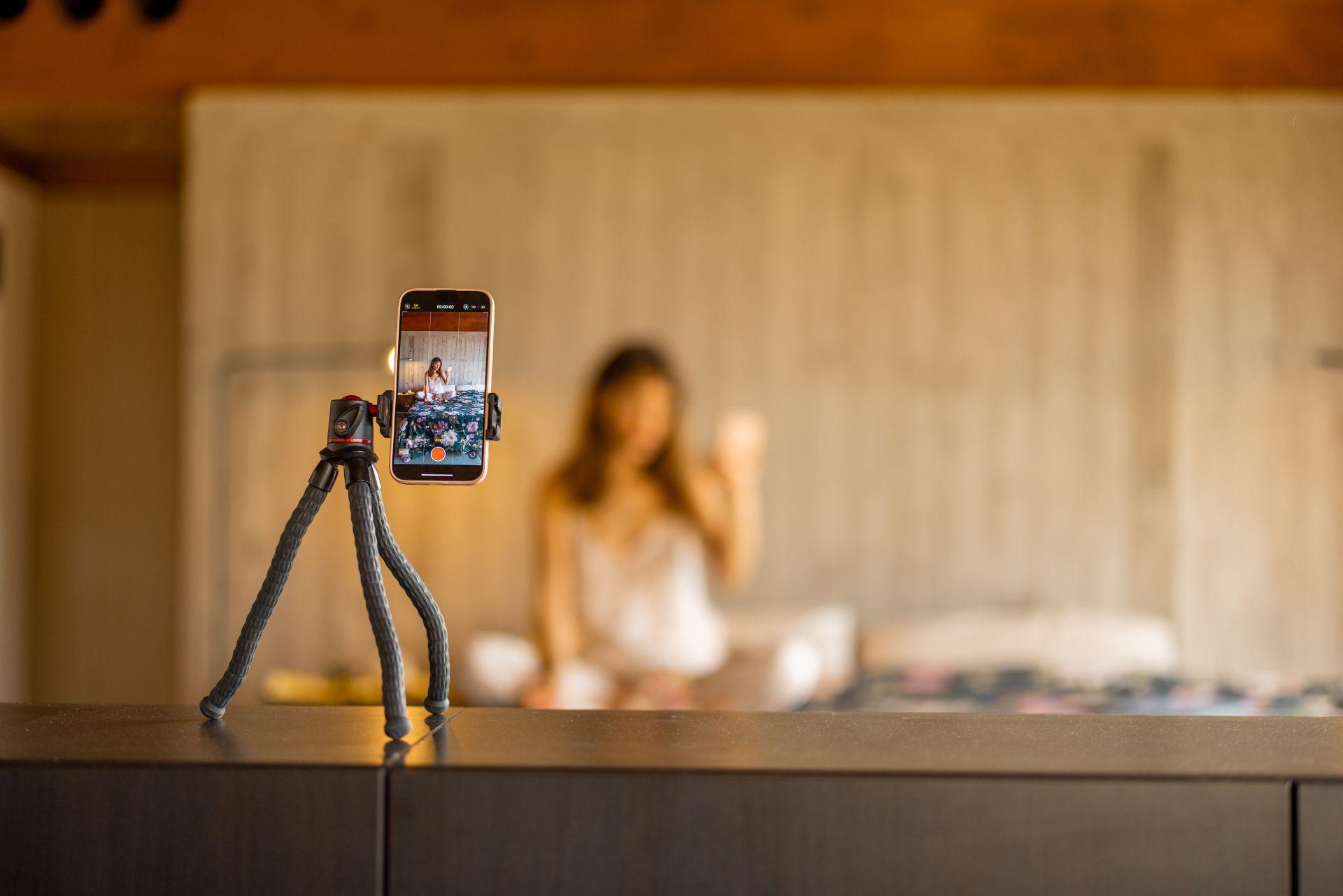 Creator filming content indoors using a smartphone on a tripod, showing how brand presentation evolves with support from only fans managers.
